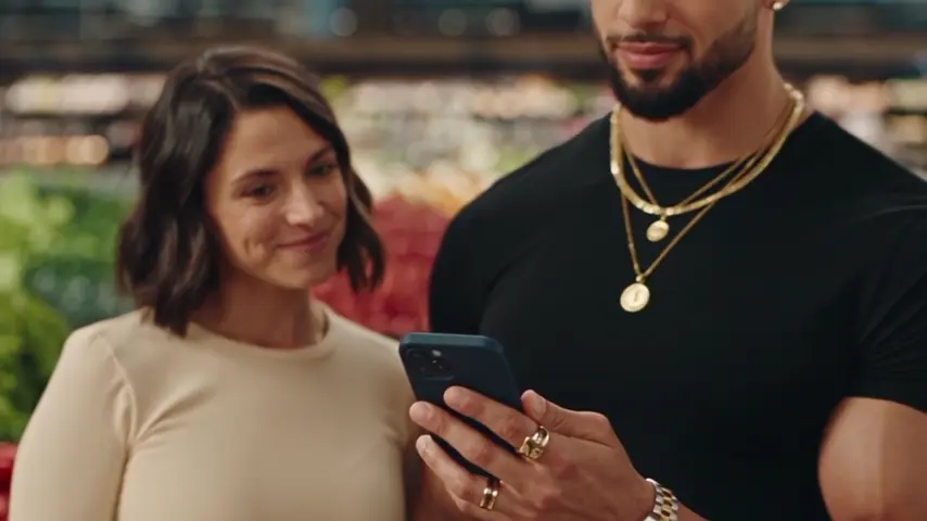 The woman smiles at the man as they look at his phone together